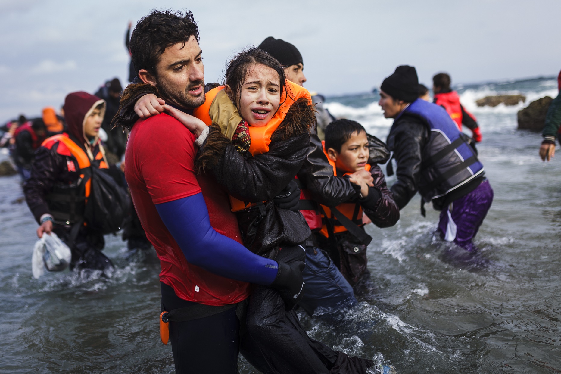 Divulgação/Acnur Voluntário segura uma menina que chegado com sua família e outros refugiados afegãos à ilha de Lesvos, na Grécia