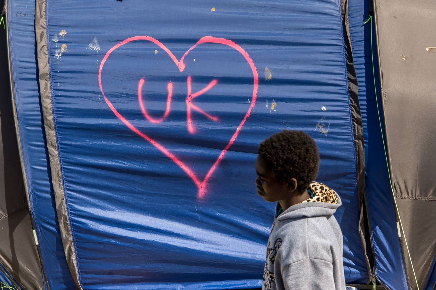 Menino passa por tenda em campo de refugiados de Calais