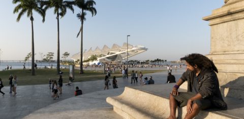 Um homem sentado num monumento observa as pessoas passeando em torno do Museu do Amanhã. Foto de Peter Bauza/DPA