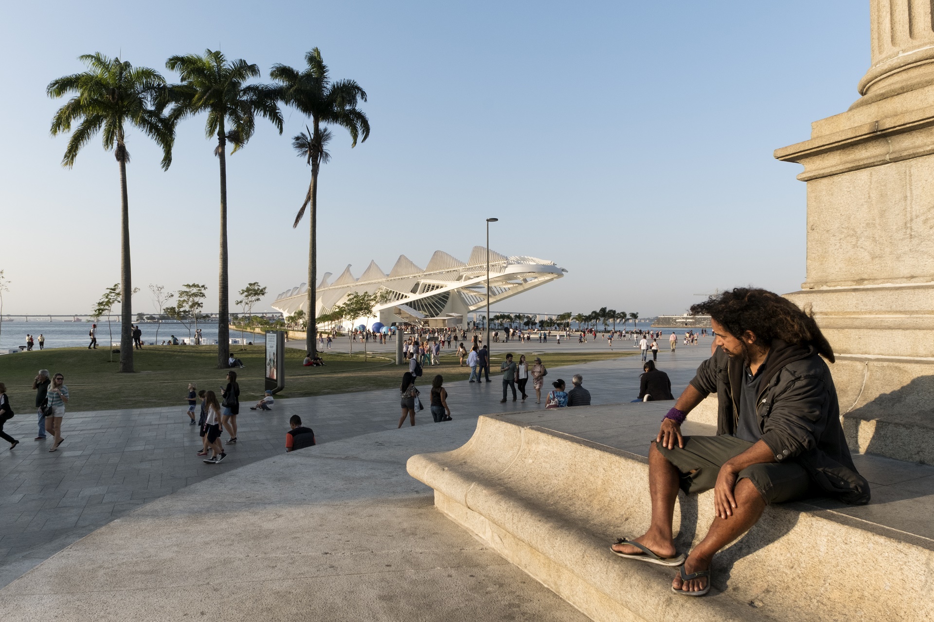 Peter Bauza/ DPA Um homem sentado num monumento observa as pessoas passeando em torno do Museu do Amanhã. Foto de Peter Bauza/DPA