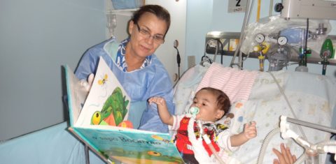 Voluntária mostra as figuras do livro para o bebê internado. Foto Divulgação