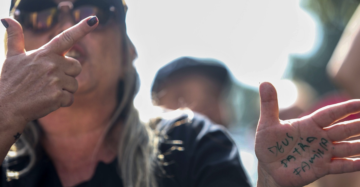 Simpatizante de Bolsonaro faz o gesto da arma com a mão e exibe as palavras Deus, Pátria e Família. Foto Miguel Schincariol