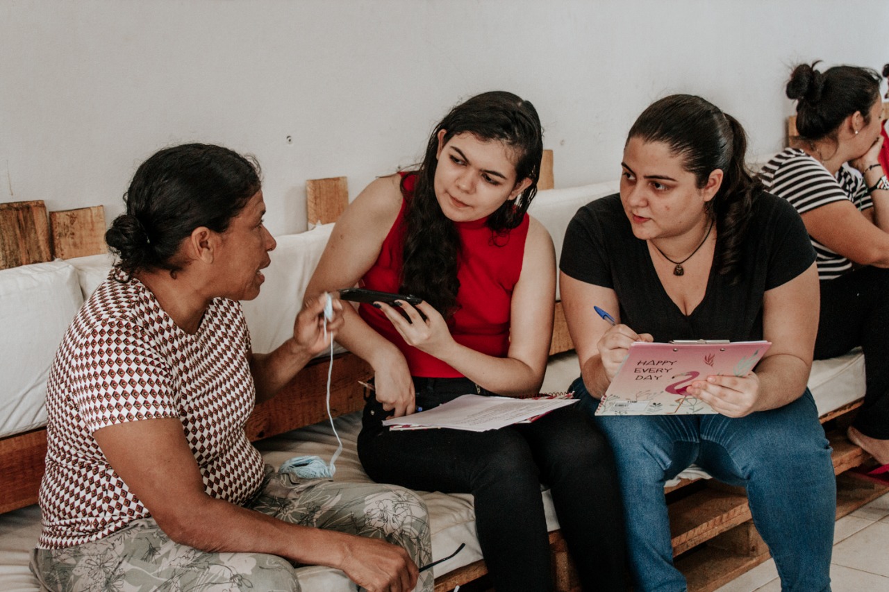 As estudantes Ana Clara Bernardes e Amanda Barros, integrantes do projeto, entrevistam venezuelana: projeto já fez entrevistas com mais de 50 migrantes e refugiados (Foto: Suedy Lorenna)