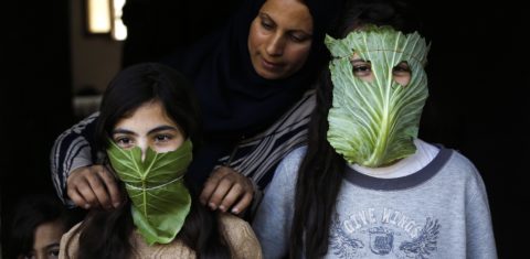 Uma mãe palestina entretém seus filhos com máscaras improvisadas de repolho enquanto cozinha em Beit Lahia, no norte da Faixa de Gaza. Foto Mohammed Abed/AFP