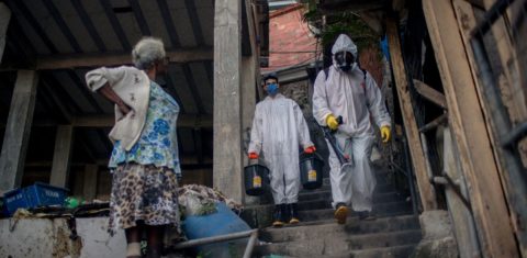 Uma mulher observa voluntários que desinfetam um beco na favela de Santa Marta, no Rio de Janeiro. Foto Mauro Pimental/AFP