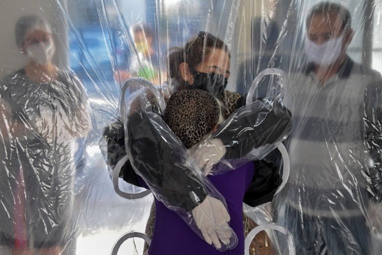 Elisabete Nagata (em cima) abraça sua cunhada Luiza Nagata, de 76 anos, através de uma cortina de plástico transparente em um lar de idosos em São Paulo. Foto Nelson Almeida/AFP