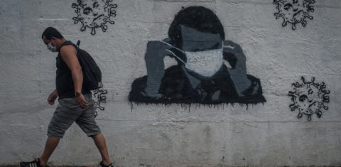 Homem de máscara passa em frente ao grafite feito pelos coletivos dos artistas Nogenta e contraconsiencia, no Rio Comprido. As imagens representam o presidente Bolsonaro. Foto Allan Carvalho/NurPhoto