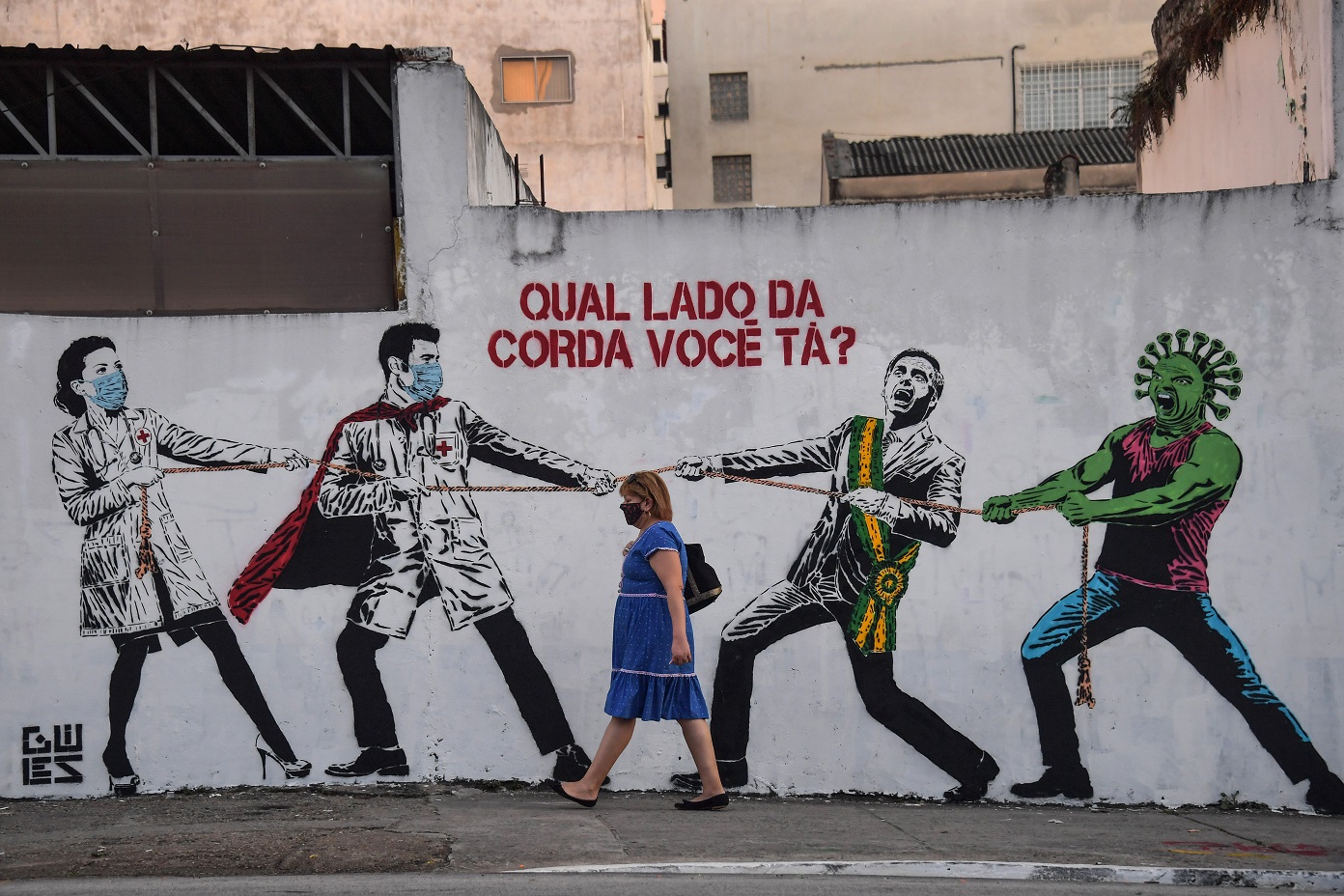 Foto Nelson Almeida/AFP Em São Paulo, mulher passa em frente a um grafiti representando a batalha contra o coronavírus: "De que lado você está?". Foto Nelson Almeida/AFP