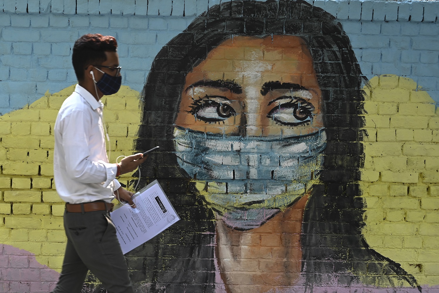 Em Nova Delhi, na Índia, homem passa por um dos muitos murais em alusão à pandemia do coronavírus. Foto Sajjad Hussain/AFP