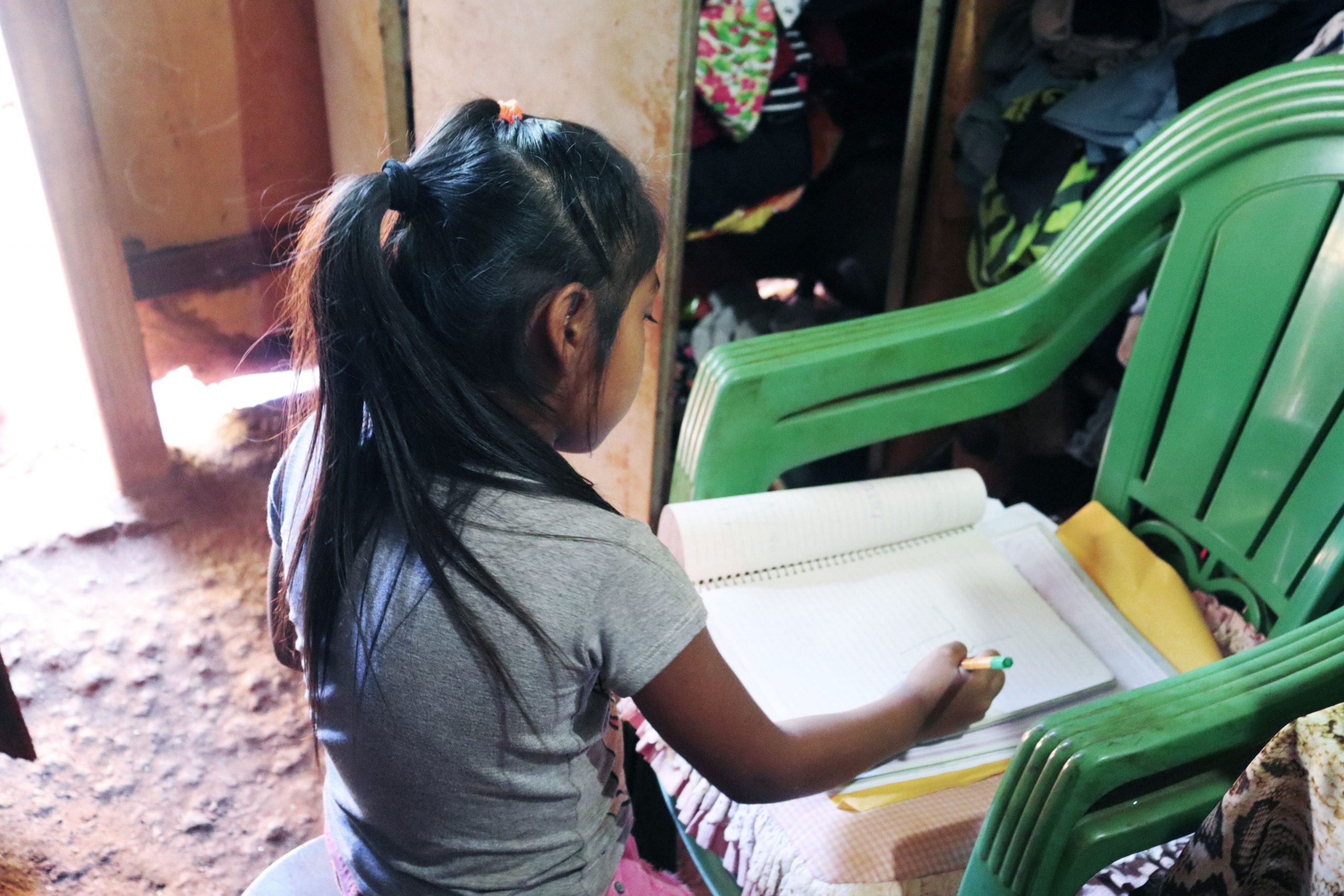Menina Terena faz a lição em cadeira improvisada como mesa: um dos poucos cantos iluminados da casa. Foto de Ethieny Karen