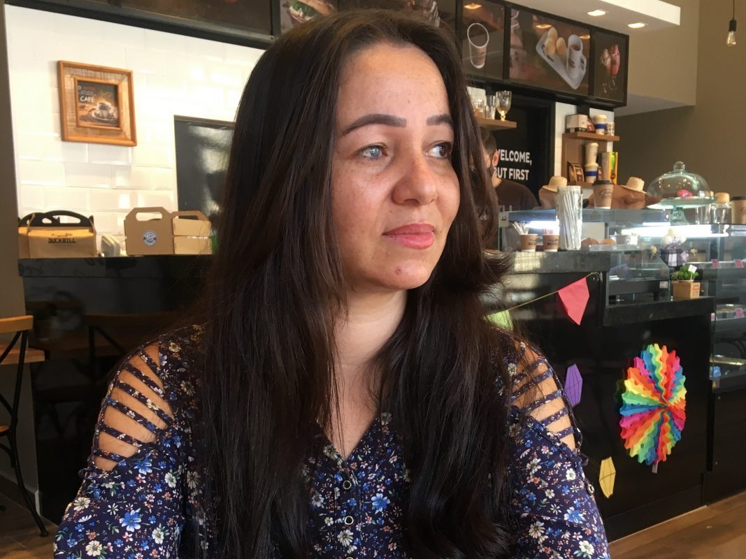 Luana Ribeiro é uma pessoa com deficiência visual que mora no interior de São Paulo. Tem cabelos longos e está sentada na área interna de uma cafeteria