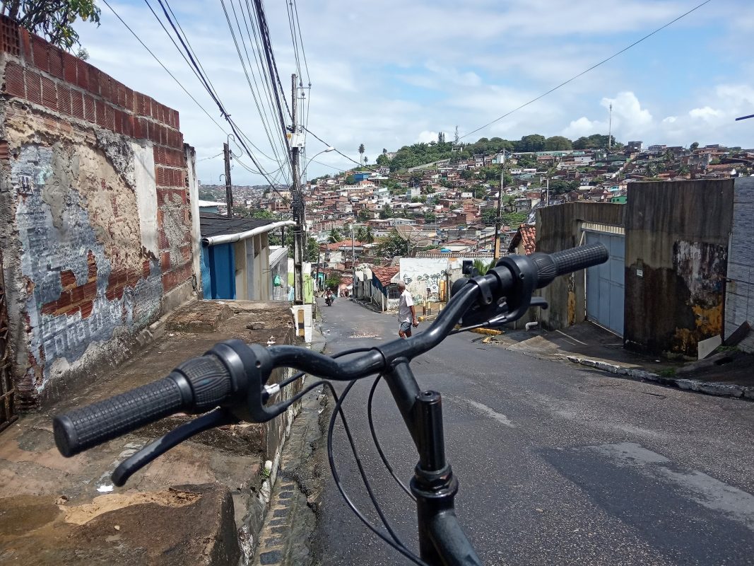 Guidão da bicicleta do repórter, em primeiro plano, com um morro de Olinda ao fundo