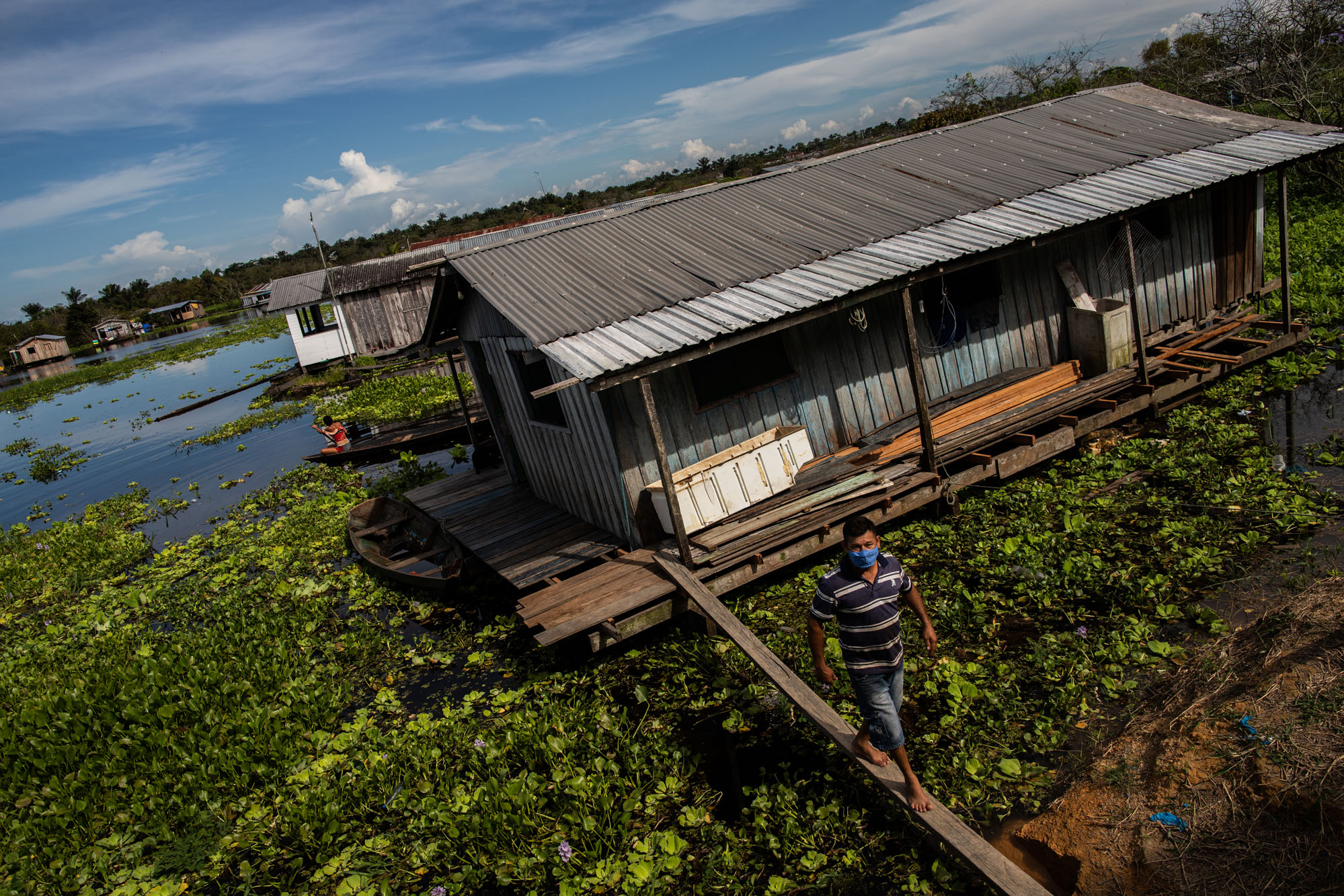 Em Iranduba (AM), Dedé Batista Pinto caminha sobre uma viga de madeira ao deixar sua sua residência flutuante na vila do Cacau Pirêra: "Final do mês passado mesmo eu matei uma cobra dentro de casa" (Foto: Raphael Alves/Amazônia Real)