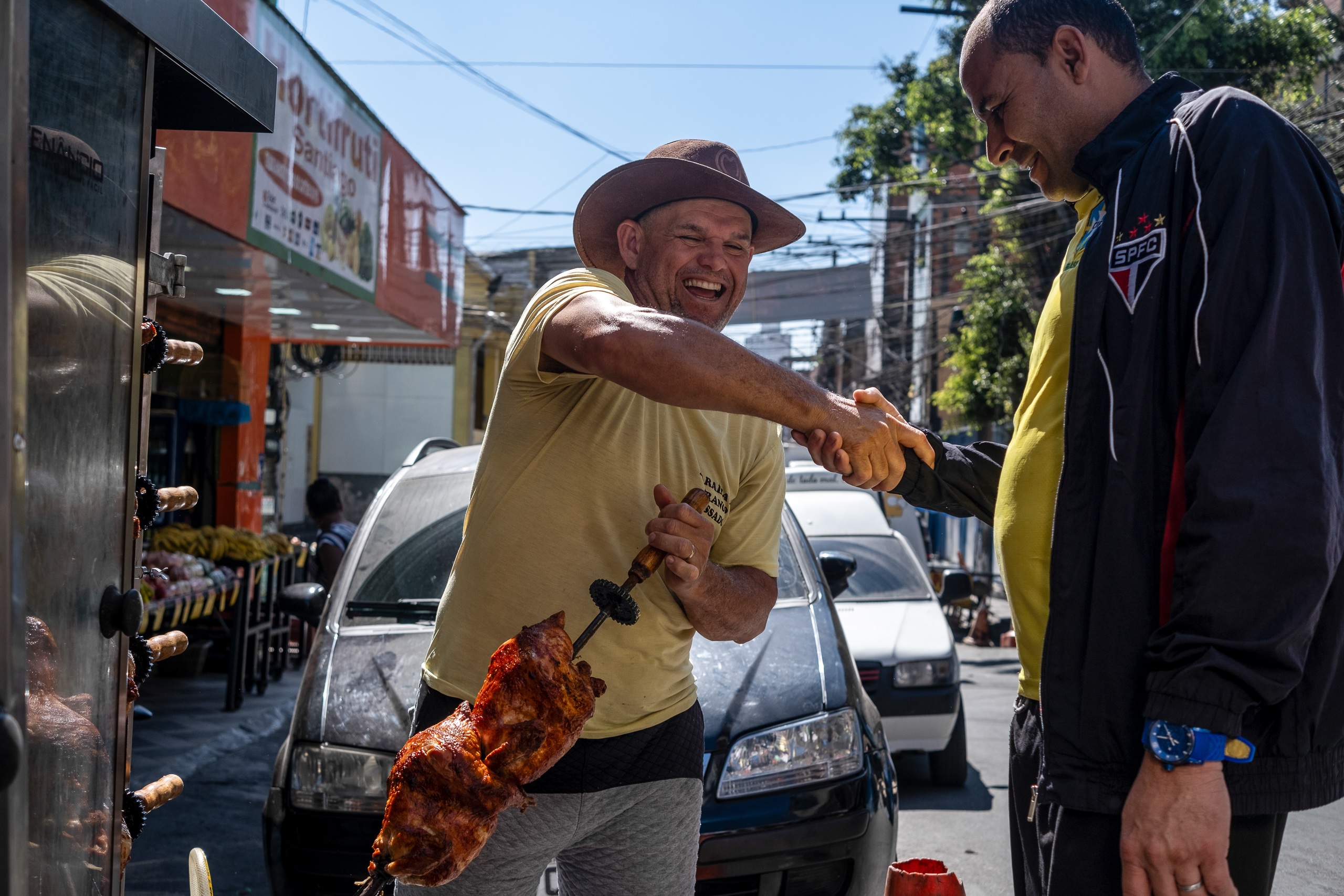 Geanes Maria de Souza, dono de banca de carne e frango assado na favela de Paraisópolis, cumprimenta cliente. Os moradores do bairro voltaram a consumir carne — sobretudo bovina — após uma queda nos preços em 2023. Foto Dan Agostini / Diálogo Chino