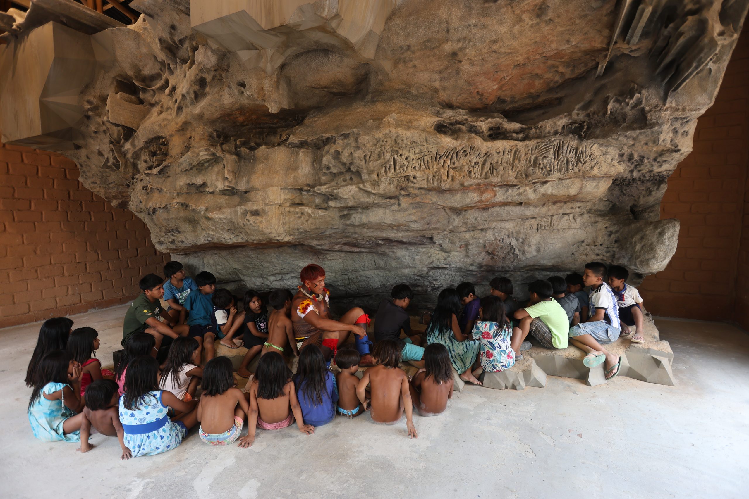 Crianças aprendendo sobre a história do guerreiro Kamukuwaká com a réplica da gruta em 3D instalada no Centro Cultural e de Monitoramento Territorial da aldeia Ulupuwene. (Alaor Filho/ Fotos Públicas)