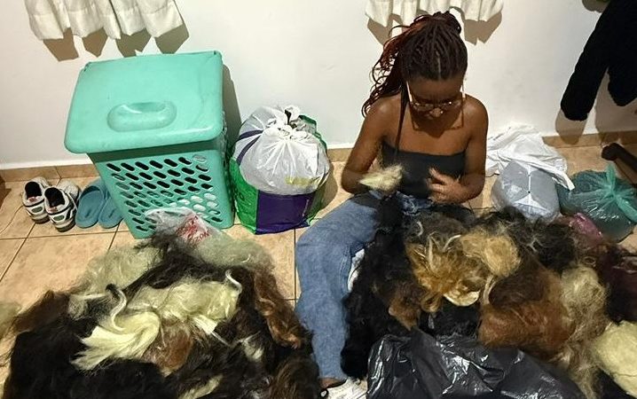 Foto colorida de Vitória ao lado de sacolas com cabelo sintético