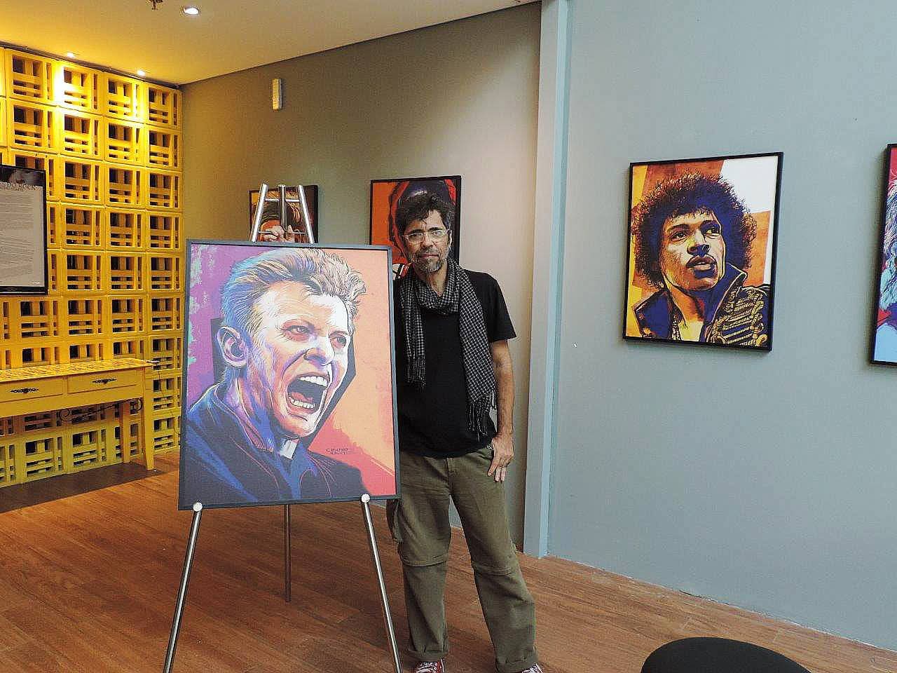 Foto colorida de Claudio Duarte ao lado de quadro com caricatura