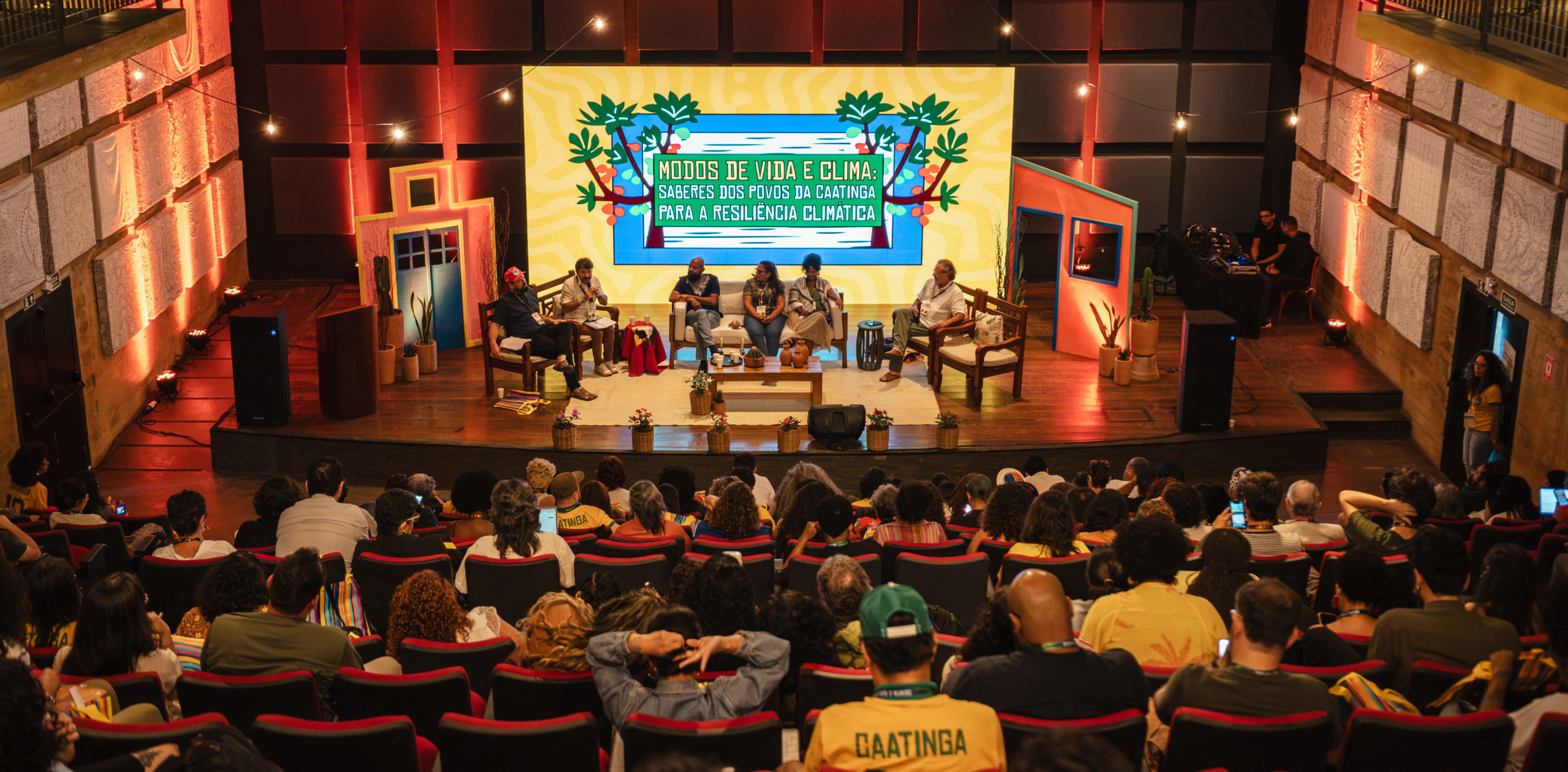 Foto colorida do painel: Modos de vida e clima, que abriu os debates da segunda edição da semana do clima na Caatinga, no Cais do Sertão, em Recife. Na imagem, aparecem os painelistas no centro e o público de costas, assistindo o evento.